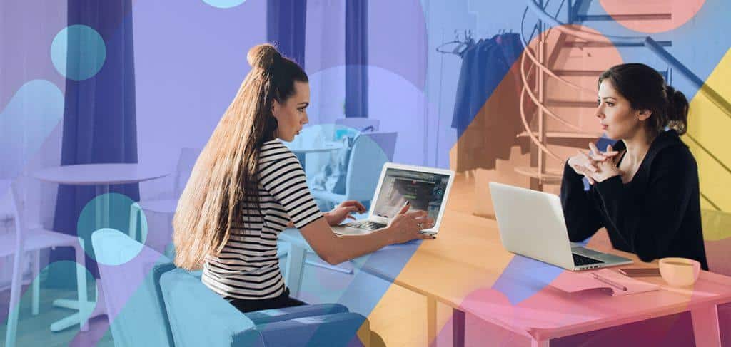 Two women sit at a table, each with a laptop. One is typing, while the other is listening intently. The colorful, abstract background includes geometric shapes and patterns.