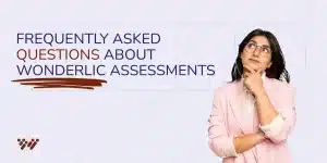 A woman in a pink blazer, hand on chin, exudes thoughtfulness. On the left, geometric lines highlight the text: "Frequently Asked Questions About Wonderlic Assessments.