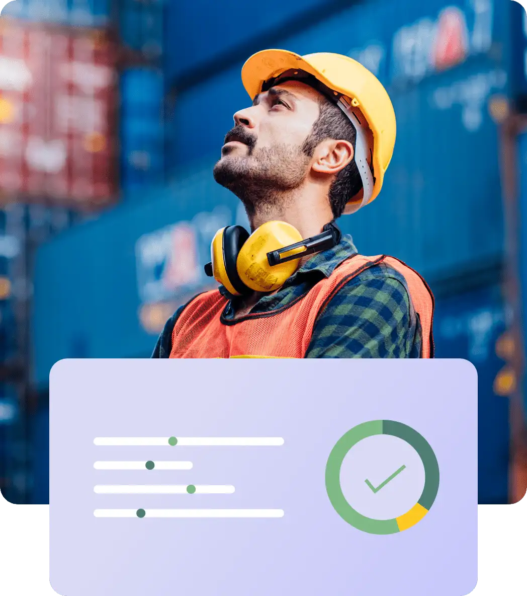 A construction worker wearing a yellow hard hat and earmuffs looks upward. Dressed in an orange safety vest and a checkered shirt, he's standing in front of stacked shipping containers. In the foreground, there is a graphic showing a progress chart and a checkmark, symbolizing the Hiring Assessment process.
