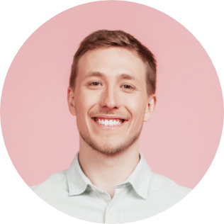 A man with short light brown hair is smiling broadly against a pastel pink background. He is wearing a light-colored button-up shirt and inviting you to get started with a Wonderlic demo. The image is circular.