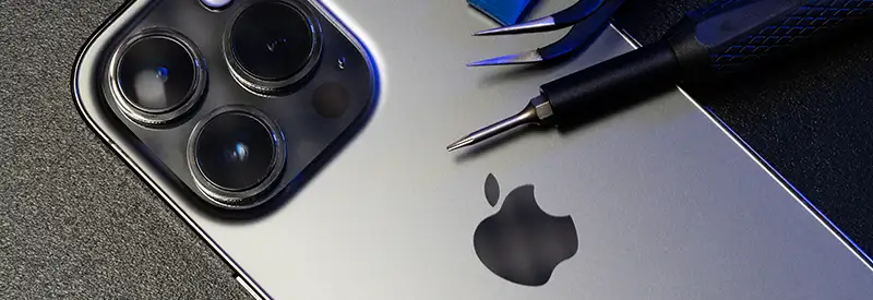 A close-up of the back of a silver iPhone with three camera lenses, placed next to precision screwdrivers and tools on a dark surface, highlights the Apple logo—symbolizing innovation fostered through strong team dynamics.