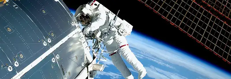An astronaut in a white spacesuit floats outside a spacecraft, collaborating on exterior repairs—a testament to strong team dynamics—with Earth’s blue and white surface, a solar panel, and parts of the space station visible in the background.