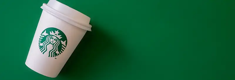 A white Starbucks coffee cup with a lid and the green mermaid logo lies tilted on a solid green background, evoking a vibrant energy reminiscent of positive team dynamics.