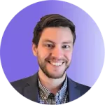 A smiling man with short brown hair and a beard, wearing a dark blazer over a checkered shirt, is pictured in front of a purple gradient background, embodying the confidence that comes from effective coaching.